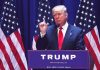 Man speaking at podium with USA flags behind him.