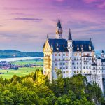 Castle surrounded by forest with scenic background.