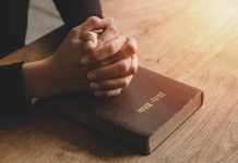 Hands praying on a Bible.