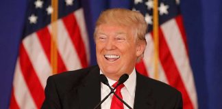 Smiling man speaking at podium with American flags.