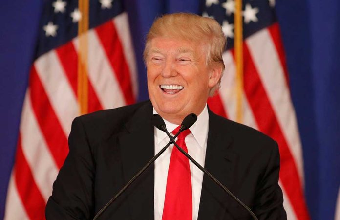 Smiling man speaking at podium with American flags.