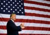 Man in front of large American flag, clapping.