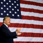 Man in front of large American flag, clapping.