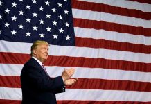 Man in front of large American flag, clapping.