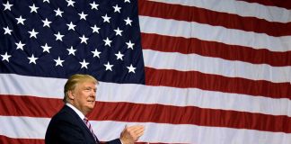 Man in front of large American flag, clapping.