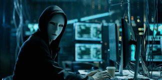 Person wearing mask and hoodie at computer desk.