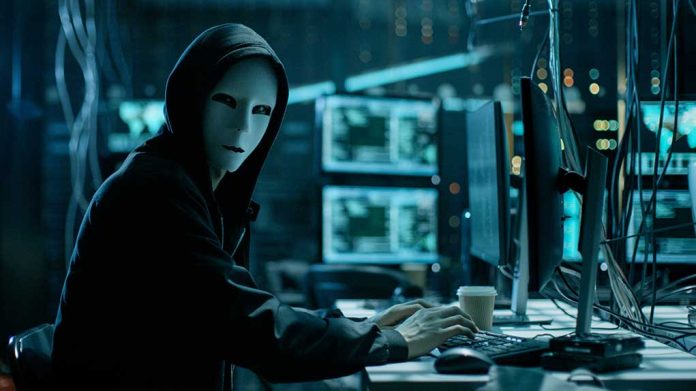 Person wearing mask and hoodie at computer desk.