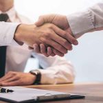 Two people shaking hands over a desk.