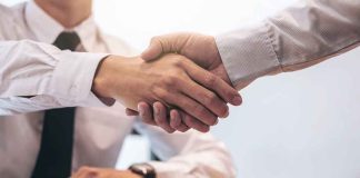 Two people shaking hands over a desk.