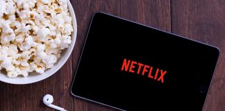 Popcorn, tablet displaying Netflix, and earphones on table.