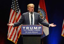 Man speaking at podium with American flags behind.