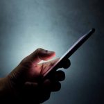 Hand holding a smartphone in the dark.