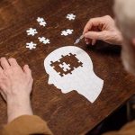 Elderly person completing head-shaped jigsaw puzzle.