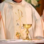 Priest in white robe with chalice and book