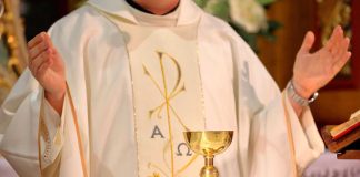 Priest in white robe with chalice and book