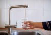 Hand filling glass with water from faucet.