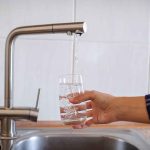 Hand filling glass with water from faucet.