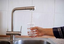 Hand filling glass with water from faucet.