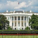 White building with columns behind a black fence.