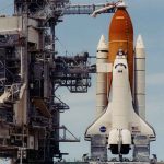 Space shuttle on launch pad with support structure.