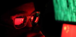 Person with glasses reflecting Chinese flag and computer screens