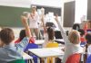 Children raising hands in classroom.