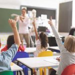 Children raising hands in classroom.