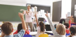 Children raising hands in classroom.