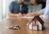 Model house and keys with couple signing documents.