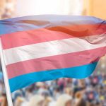 Transgender pride flag waving at outdoor event.