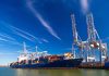 Blue cargo ship docked at port with cranes.