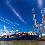 Blue cargo ship docked at port with cranes.