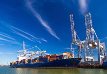 Blue cargo ship docked at port with cranes.