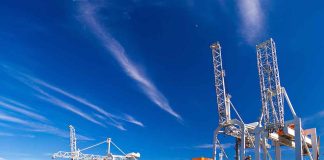 Blue cargo ship docked at port with cranes.