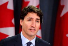 Man speaking in front of Canadian flags.