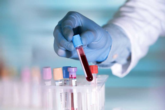 Gloved hand holding a test tube with blood.