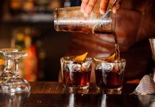 Bartender pouring cocktails into glasses with lemon garnish.