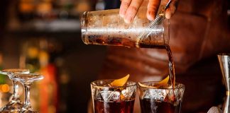 Bartender pouring cocktails into glasses with lemon garnish.