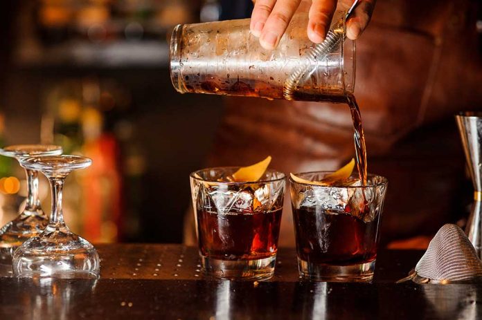 Bartender pouring cocktails into glasses with lemon garnish.