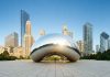 Cloud Gate sculpture with skyline of skyscrapers behind it.