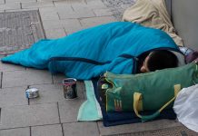 Person sleeping on sidewalk in blue sleeping bag.