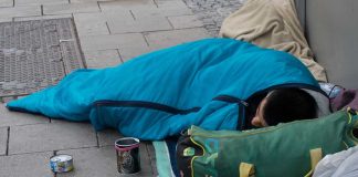 Person sleeping on sidewalk in blue sleeping bag.