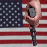 Hand holding gun with American flag background.