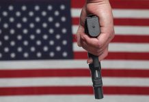 Hand holding gun with American flag background.