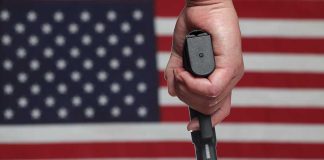 Hand holding gun with American flag background.