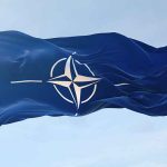 NATO flag waving against blue sky.