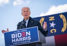 Man speaking at outdoor event with microphones and banner