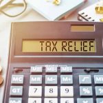 Calculator display reads "TAX RELIEF" amidst coins and glasses.