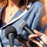 Person surrounded by microphones during an interview