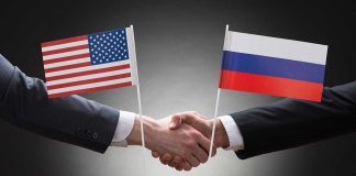 Two people shaking hands with flags displayed